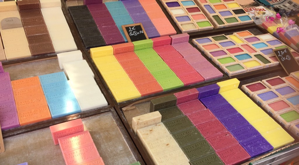 Trays of brightly coloured blocks of Marseille soap laid out in rows on a market stall.
