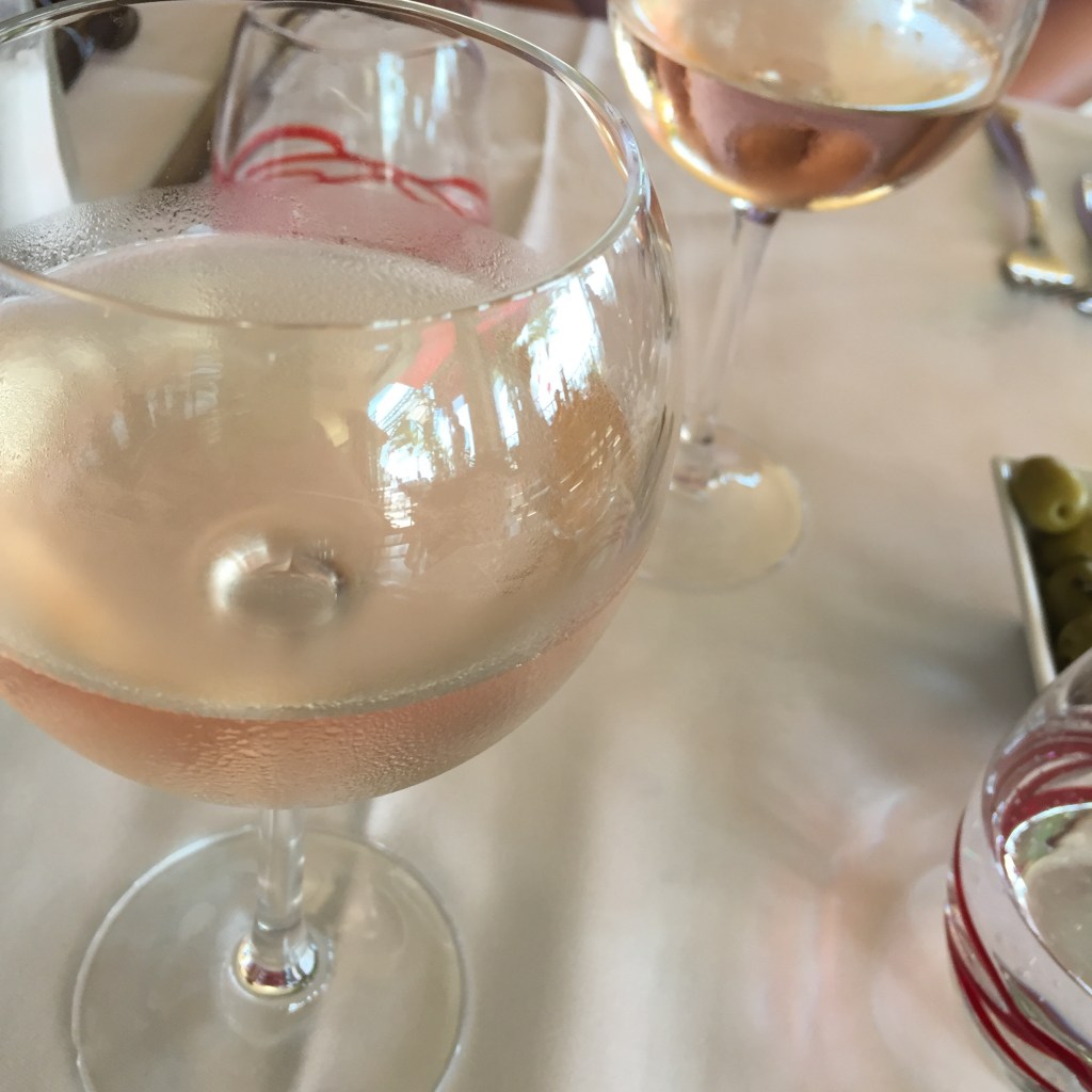 Two glasses of pale rosé on a white tablecloth, condensation on the bowls.