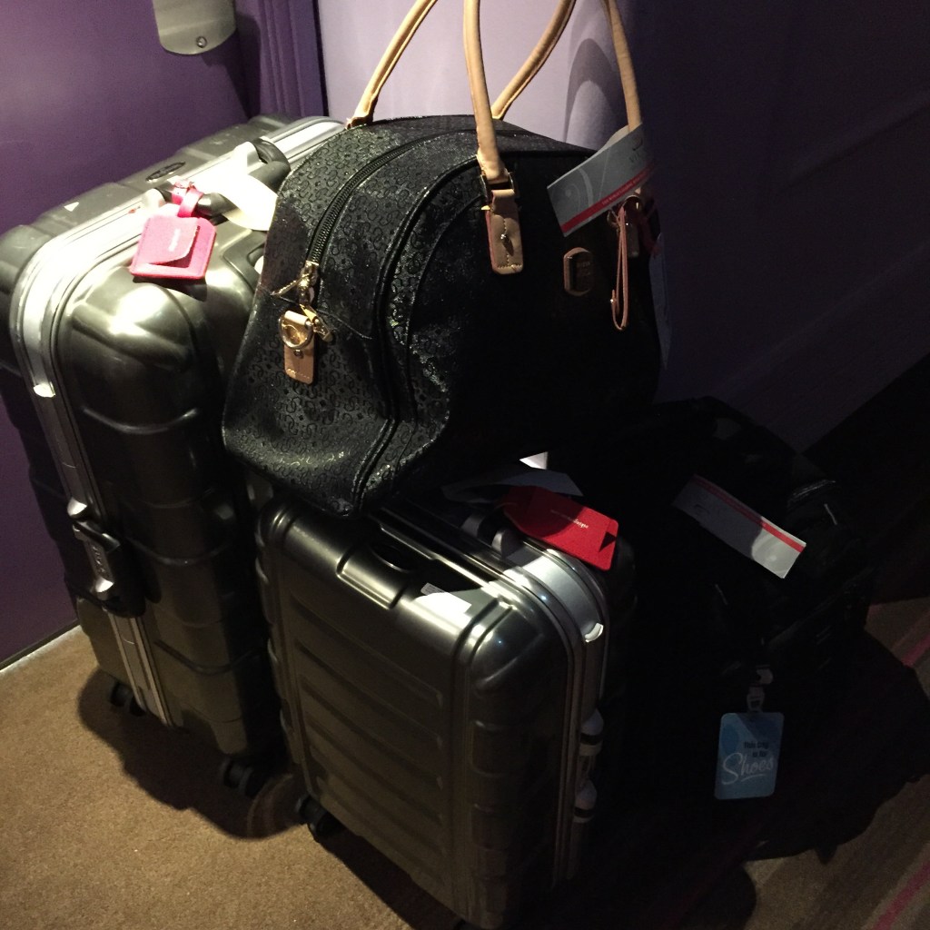 Two silver hard-shell suitcases stacked by a door with a black handbag balanced on top, luggage tags attached.