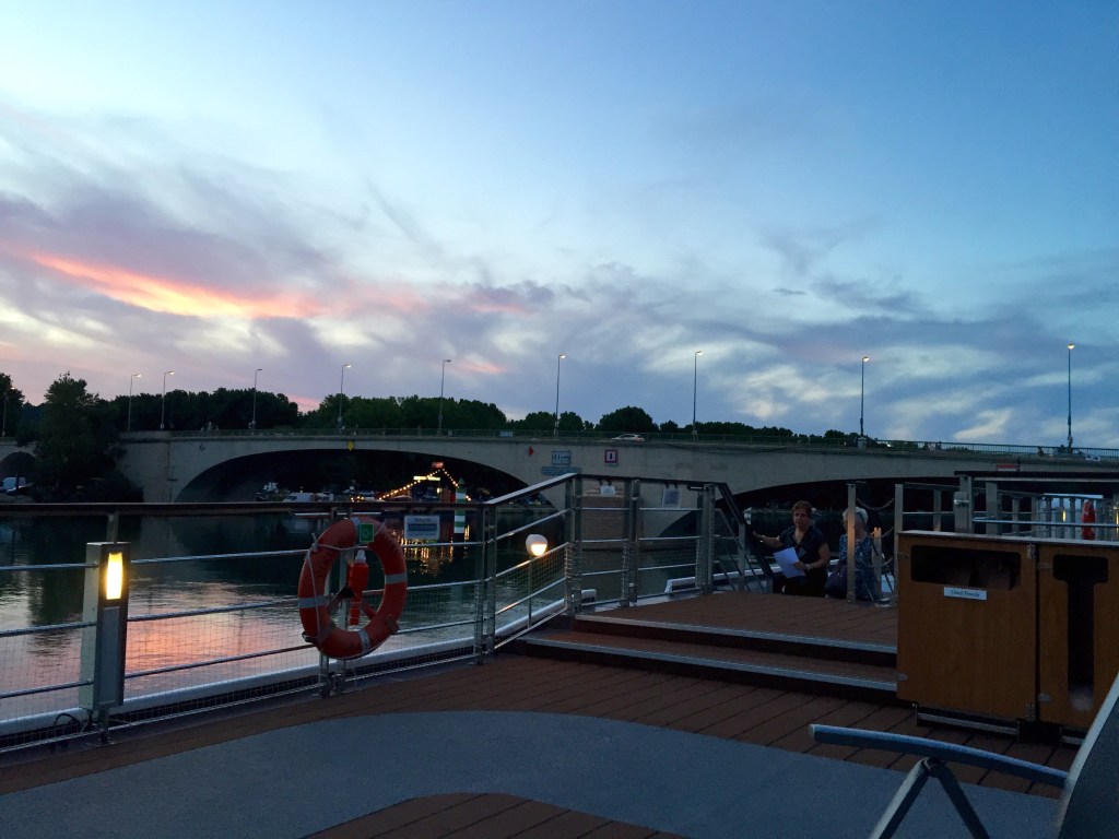 Sunset over the Rhône from the ship&rsquo;s top deck, a road bridge in silhouette and a lifebuoy on the rail.