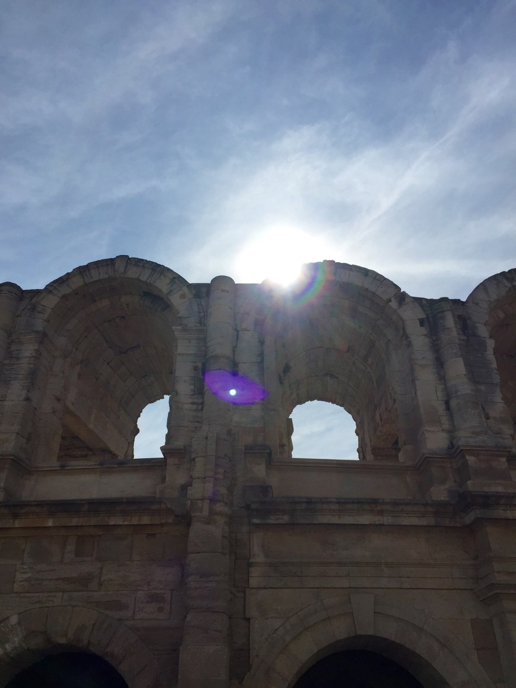 The upper arches of the Arles amphitheatre with the sun flaring through the openings.