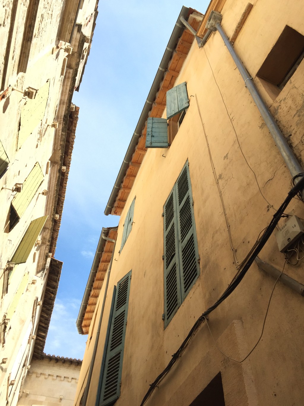 Looking steeply up a narrow Arles street at ochre facades and pale blue shutters.