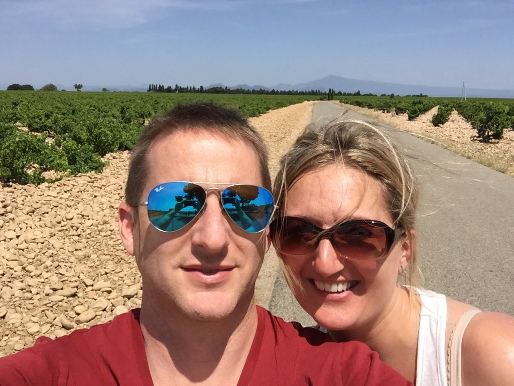Chris and Jen in sunglasses on a stony track between vine rows, the bare summit of Mont Ventoux on the horizon behind them.