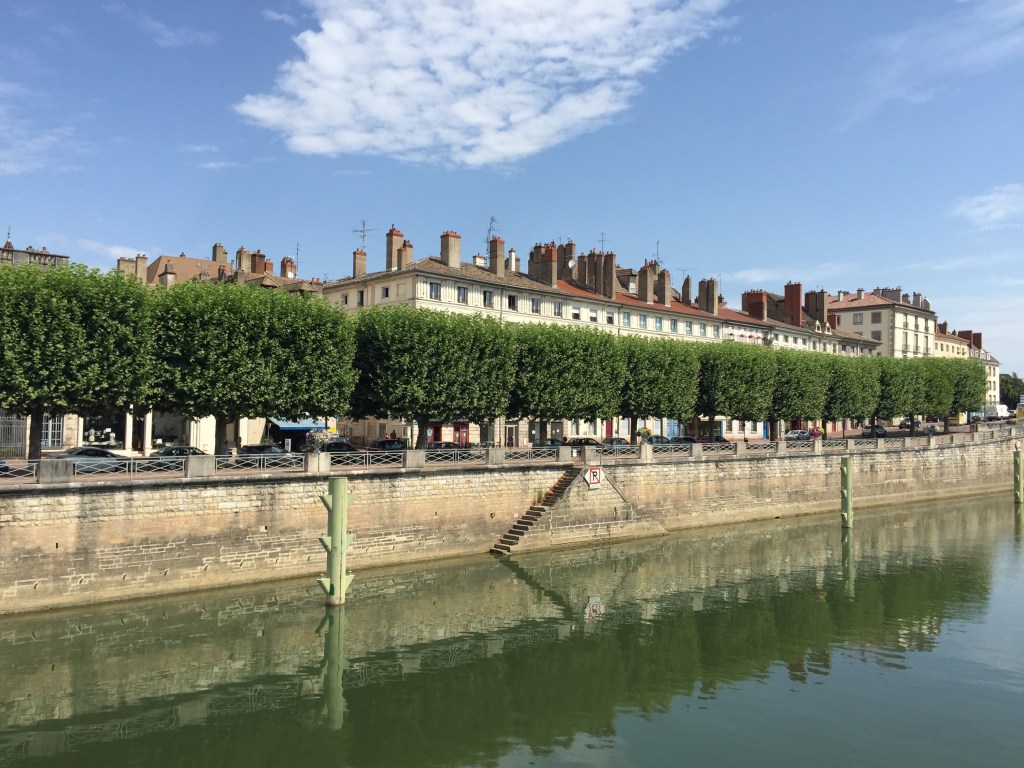 The quay at Lyon: clipped plane trees along the embankment and a long terrace of honey-coloured buildings across green water.