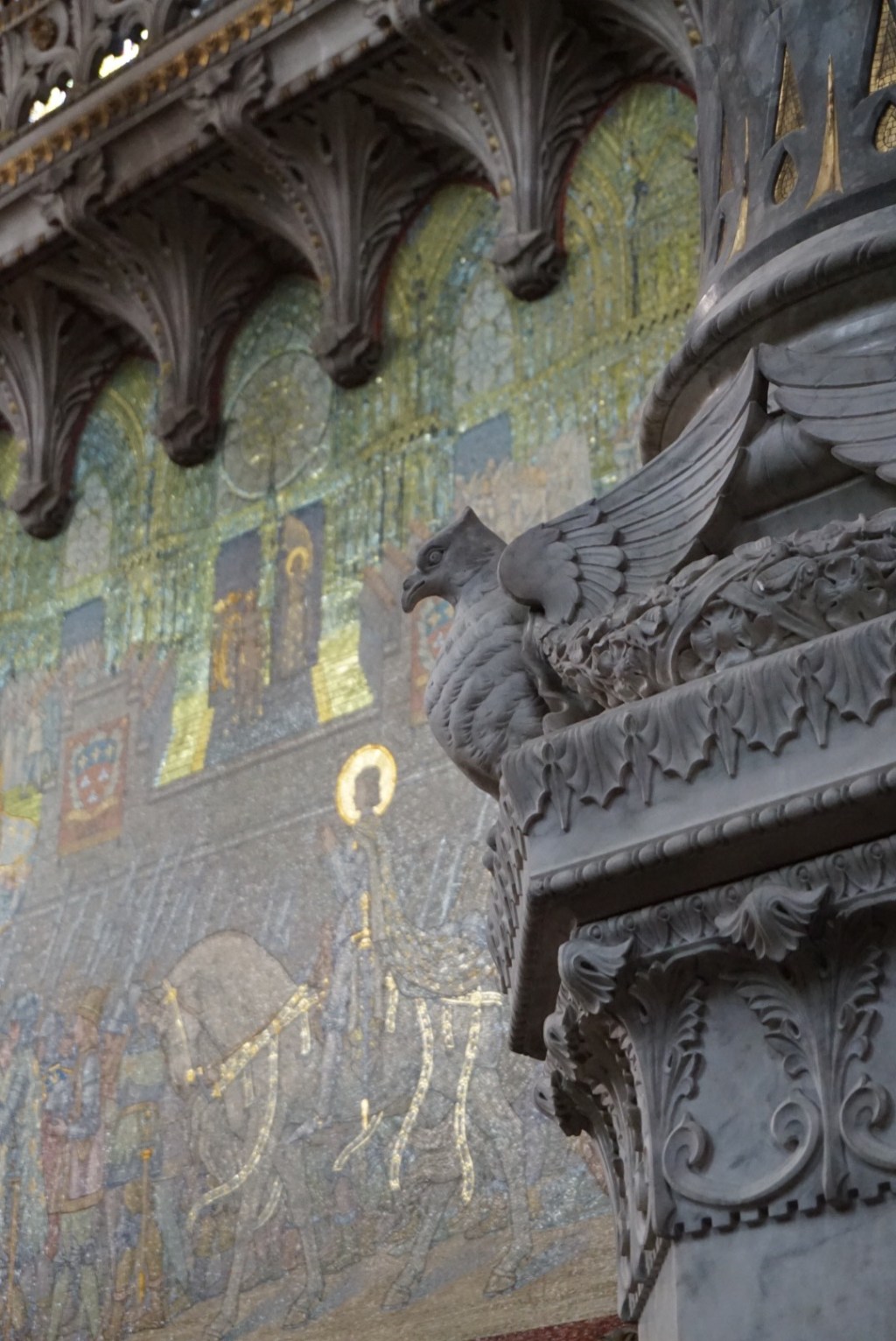 A detail of a Lyon facade: gilded mosaic panels above a carved stone cornice and a winged grotesque.