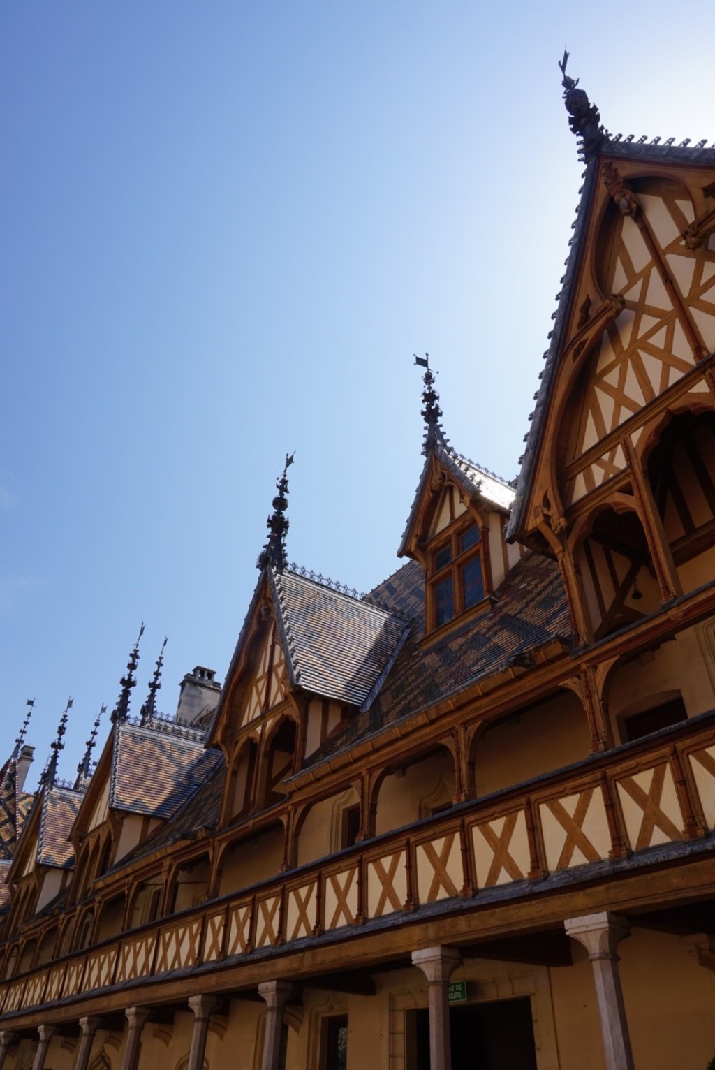 The glazed polychrome tiled roof of the Hospices de Beaune, its patterned slates and gothic dormers against a clear sky.