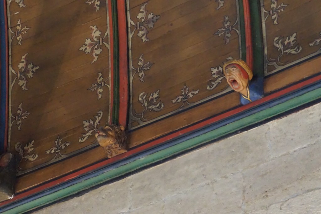 A painted wooden ceiling beam decorated with scrollwork, a small carved face projecting from it.