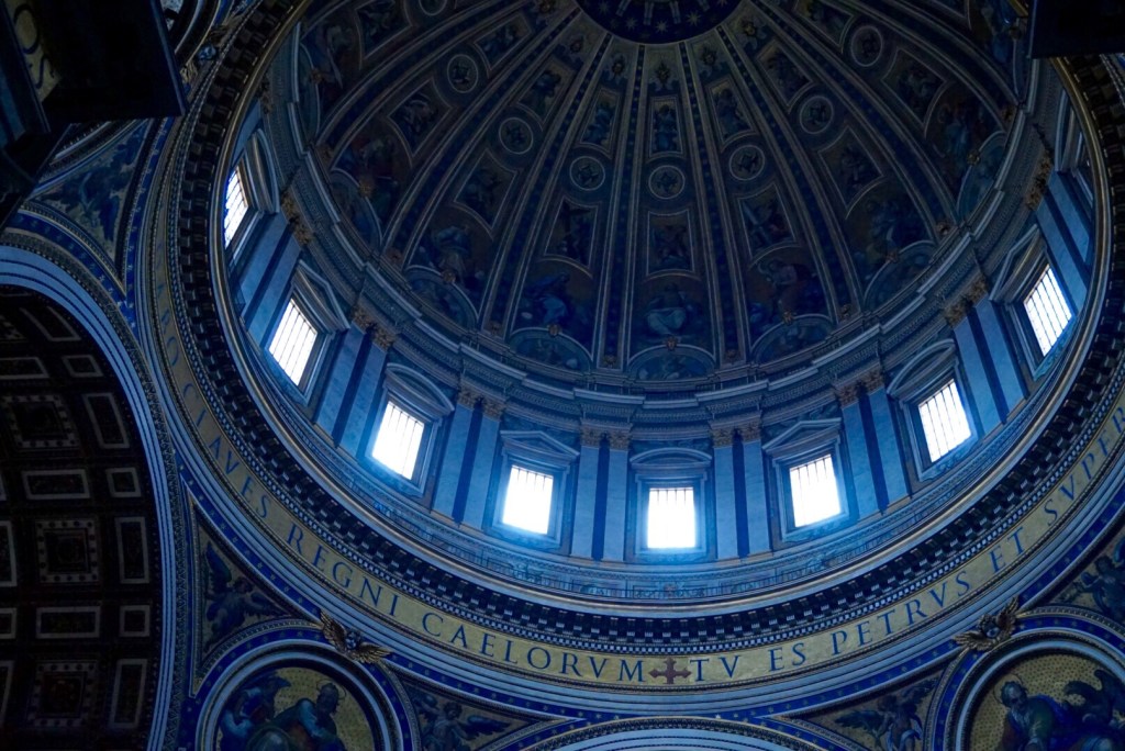 Looking straight up into Michelangelo's dome at St Peter's, a ring of windows below the gold mosaic frieze