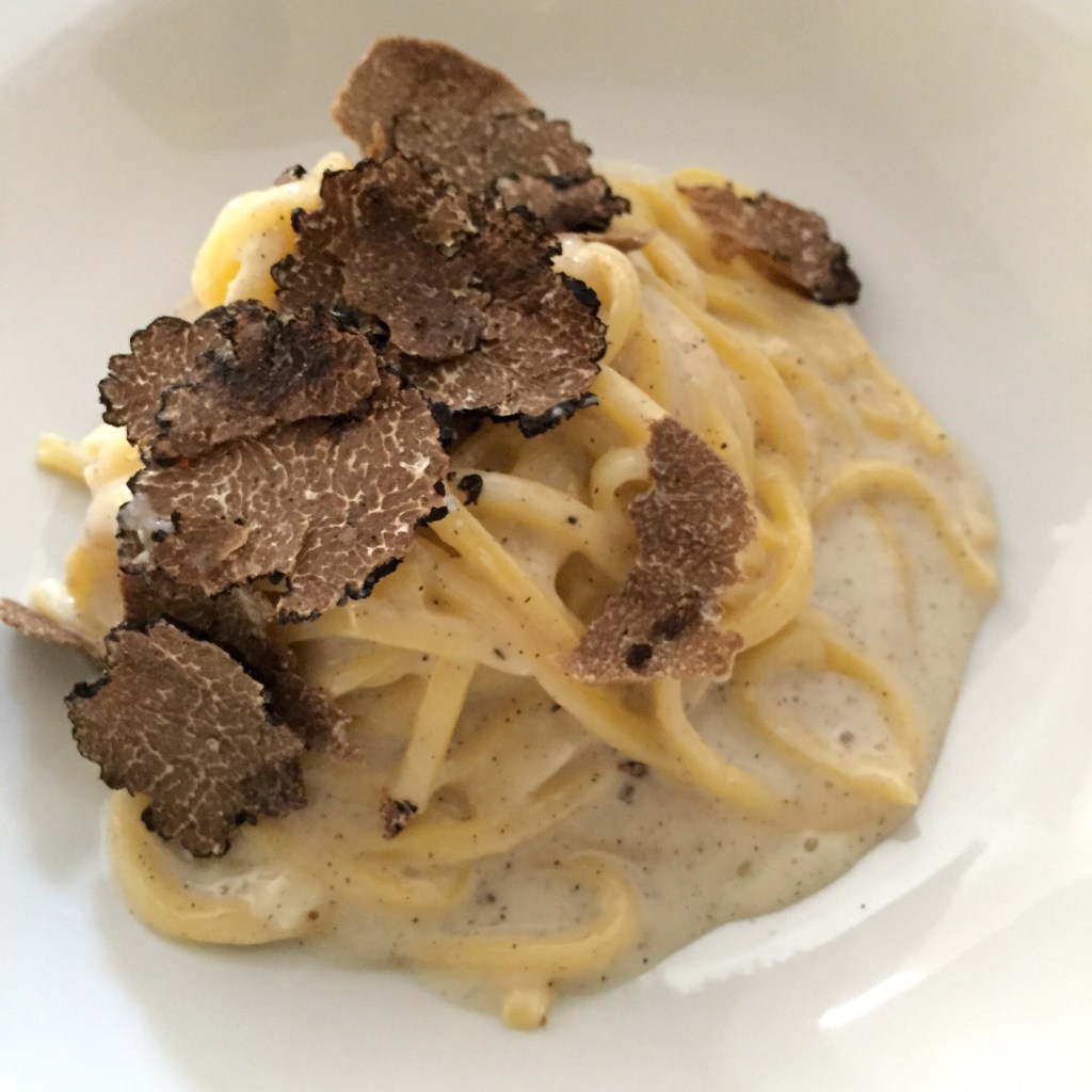 A bowl of tagliolini in a cream sauce under a generous scattering of shaved black truffle