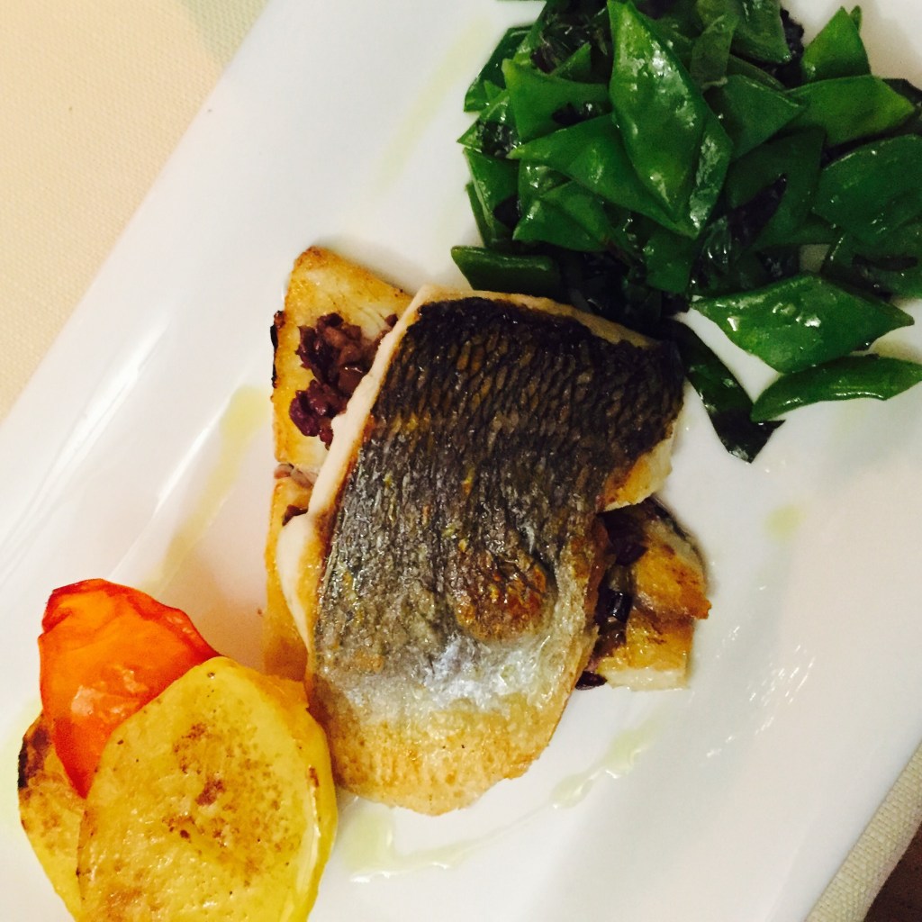 A crisp-skinned fillet of sea bass with mangetout, a roast potato and a slice of tomato