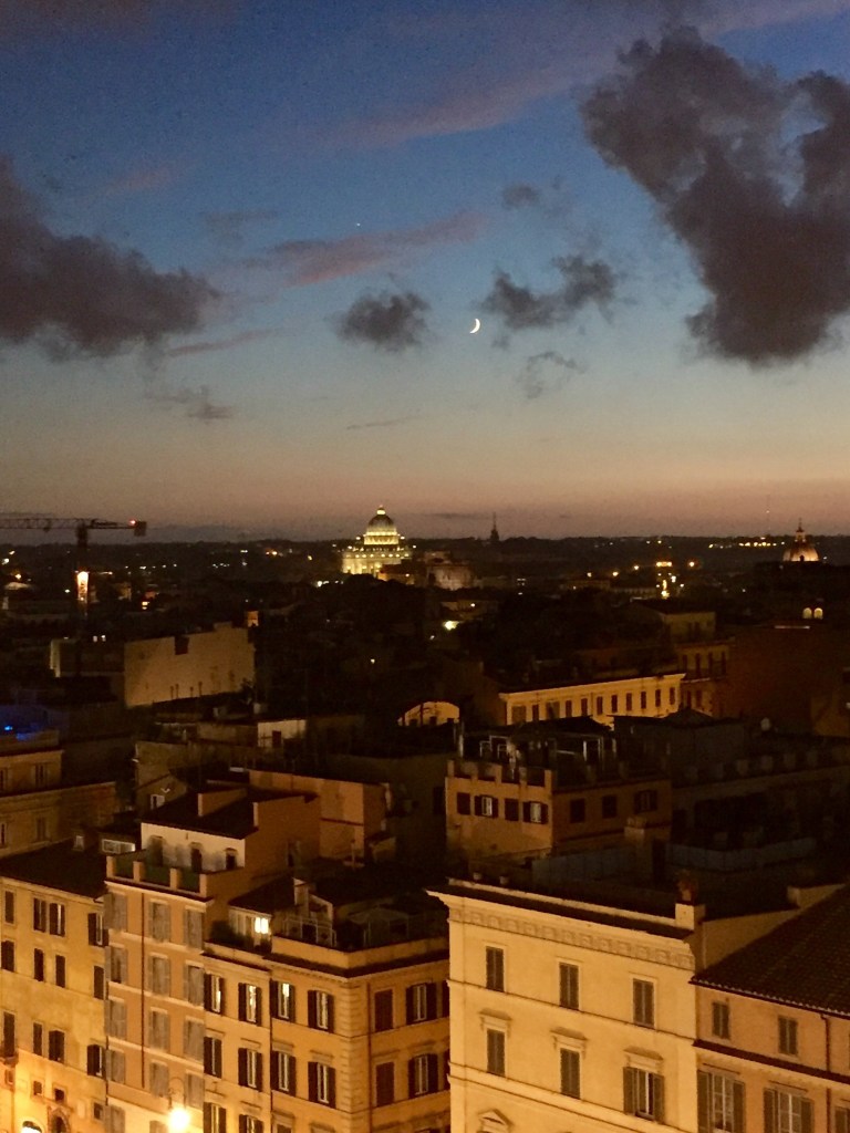 Dusk over the rooftops of Rome from a terrace, the dome of St Peter's on the skyline and a crescent moon among the clouds
