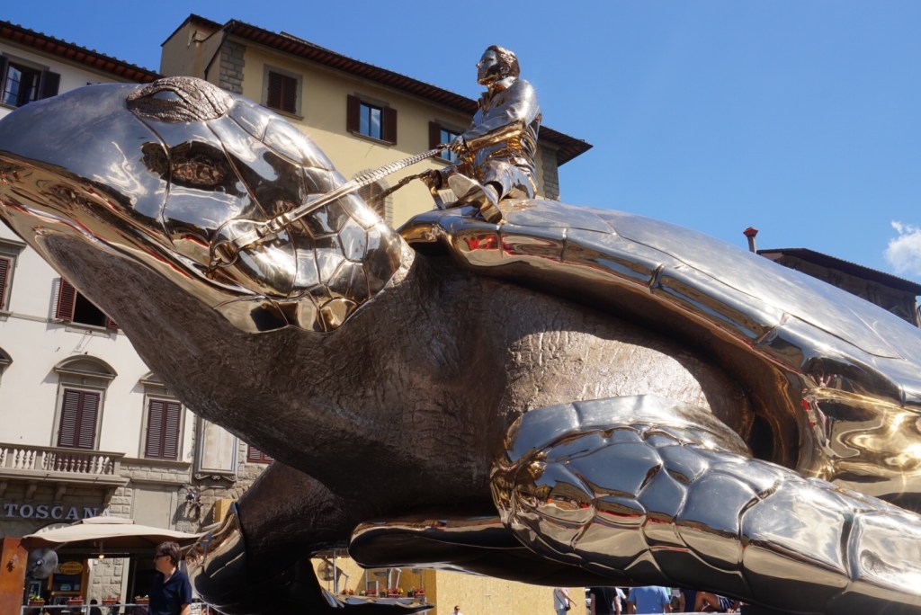 A mirror-polished sculpture of an armoured figure riding a giant tortoise in a Florence square