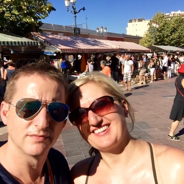 Chris and Jen at the Cours Saleya market in Nice, stalls and crowds along the street behind them