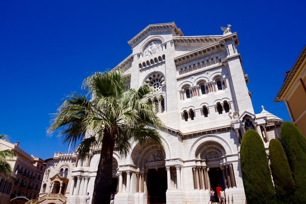 The white stone front of Monaco Cathedral behind a palm tree