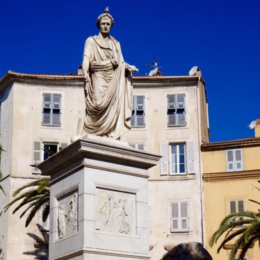 A marble statue of Napoleon in Roman dress on a tall pedestal, a stone lion couched at its base