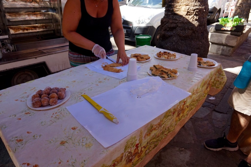 A stallholder in gloves cutting samples of pastries on a cloth-covered table at the Ajaccio market