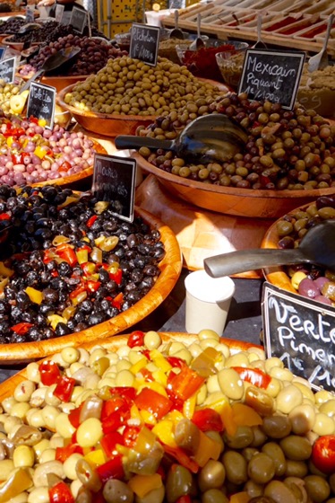 Terracotta bowls of black, green and marinated olives at a market stall, handwritten price cards propped among them
