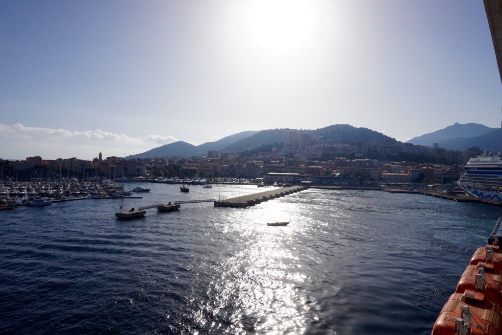 The sun low over Ajaccio harbour as the ship pulls away past the breakwater