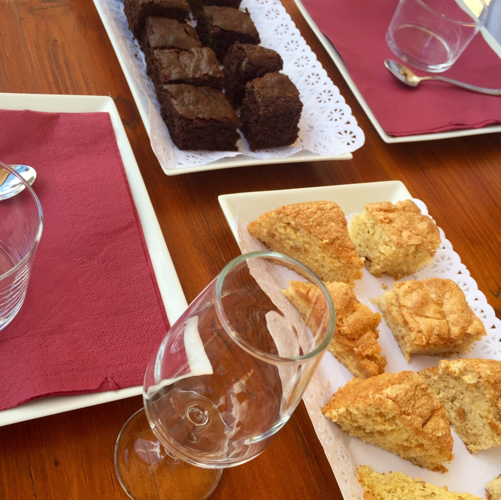 Plates of dark cake squares and golden pastry wedges set out on a tasting table with wine glasses