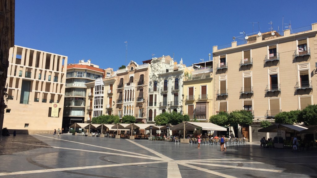 A wide paved square in Murcia, cafe awnings along one side