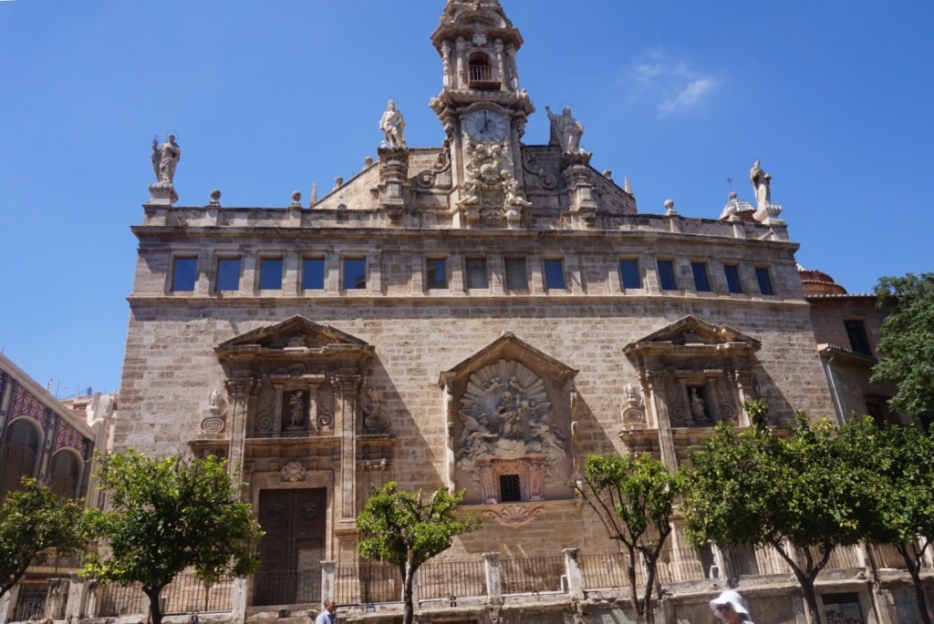 The baroque front of the church of Santos Juanes in Valencia, orange trees along the pavement