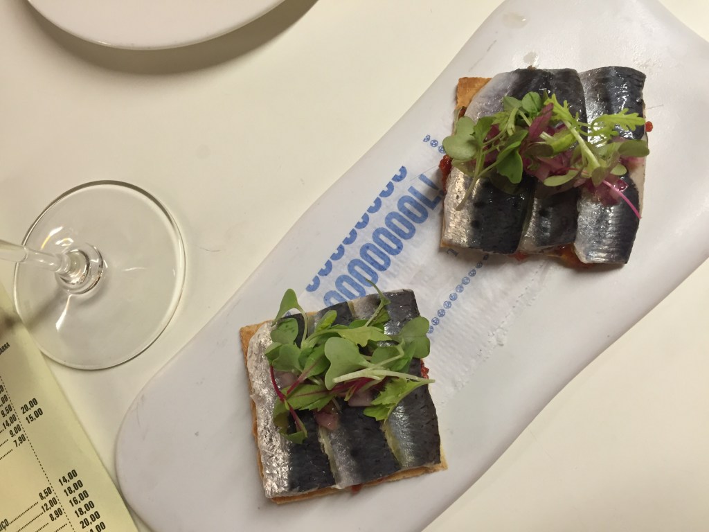 Two sardine toasts on a long white plate at dinner