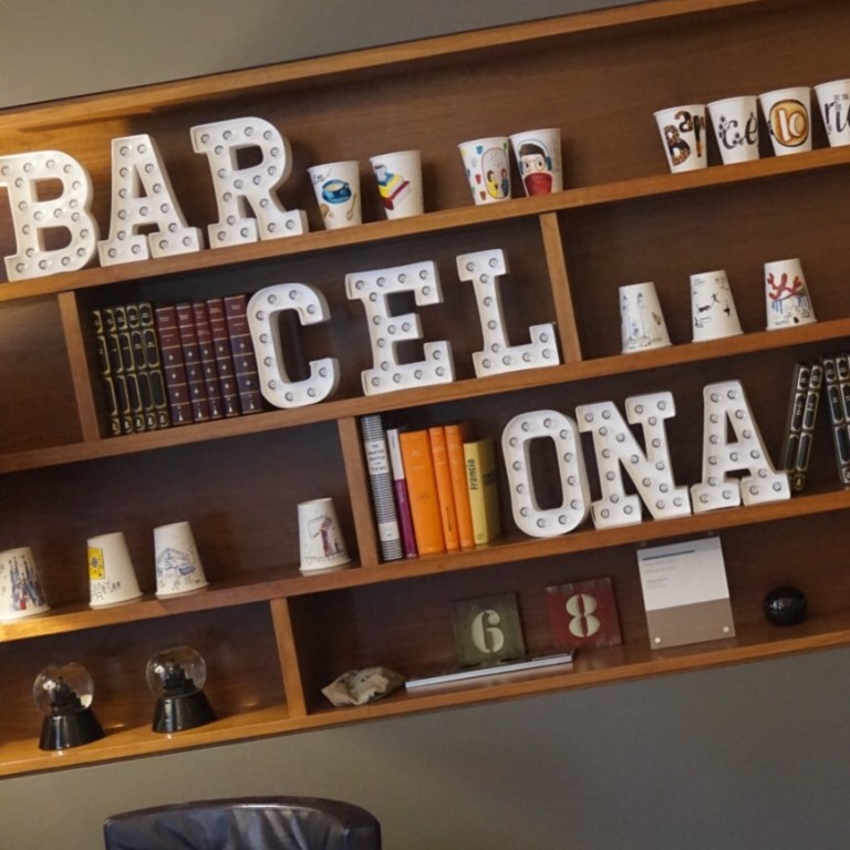 Ceramic letters spelling BARCELONA on a shelf of books and pots in the hotel lobby