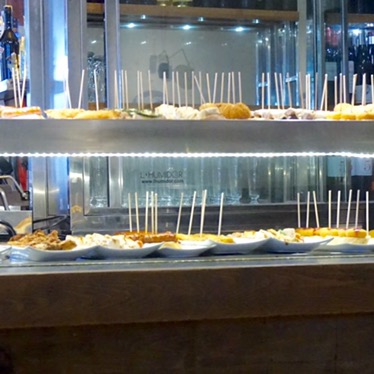 The counter of a pintxos bar, plates of skewered snacks set out along it