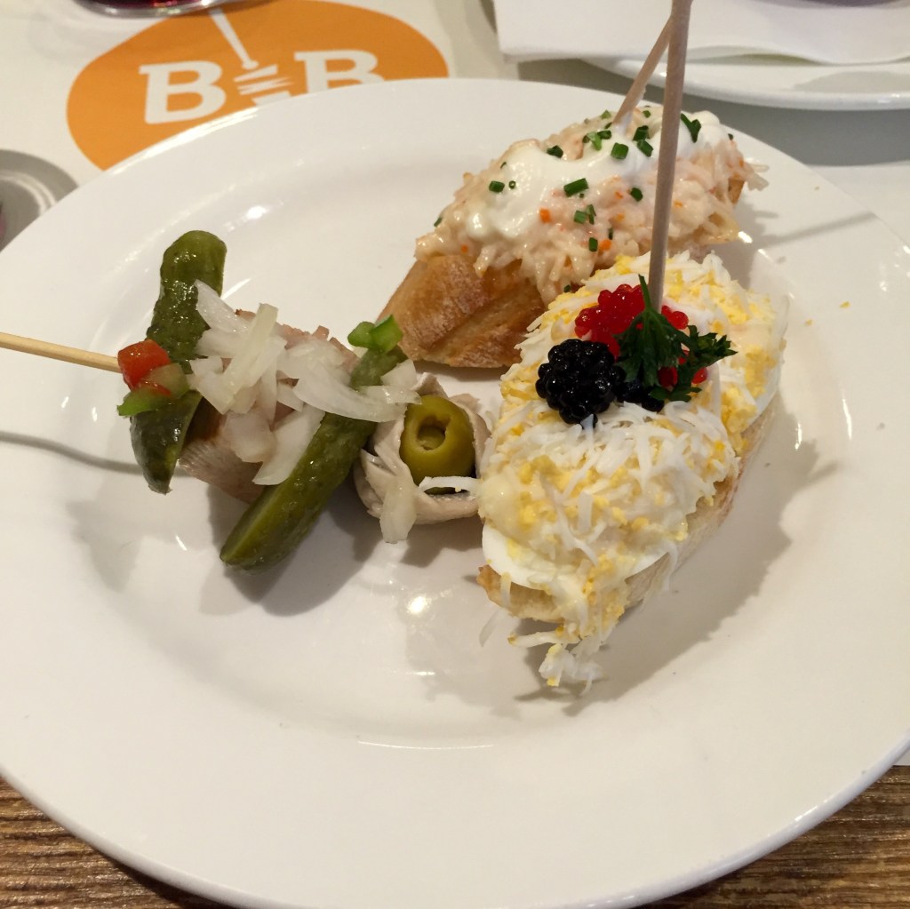 A plate of pintxos with their wooden skewers, a glass of red wine beside it