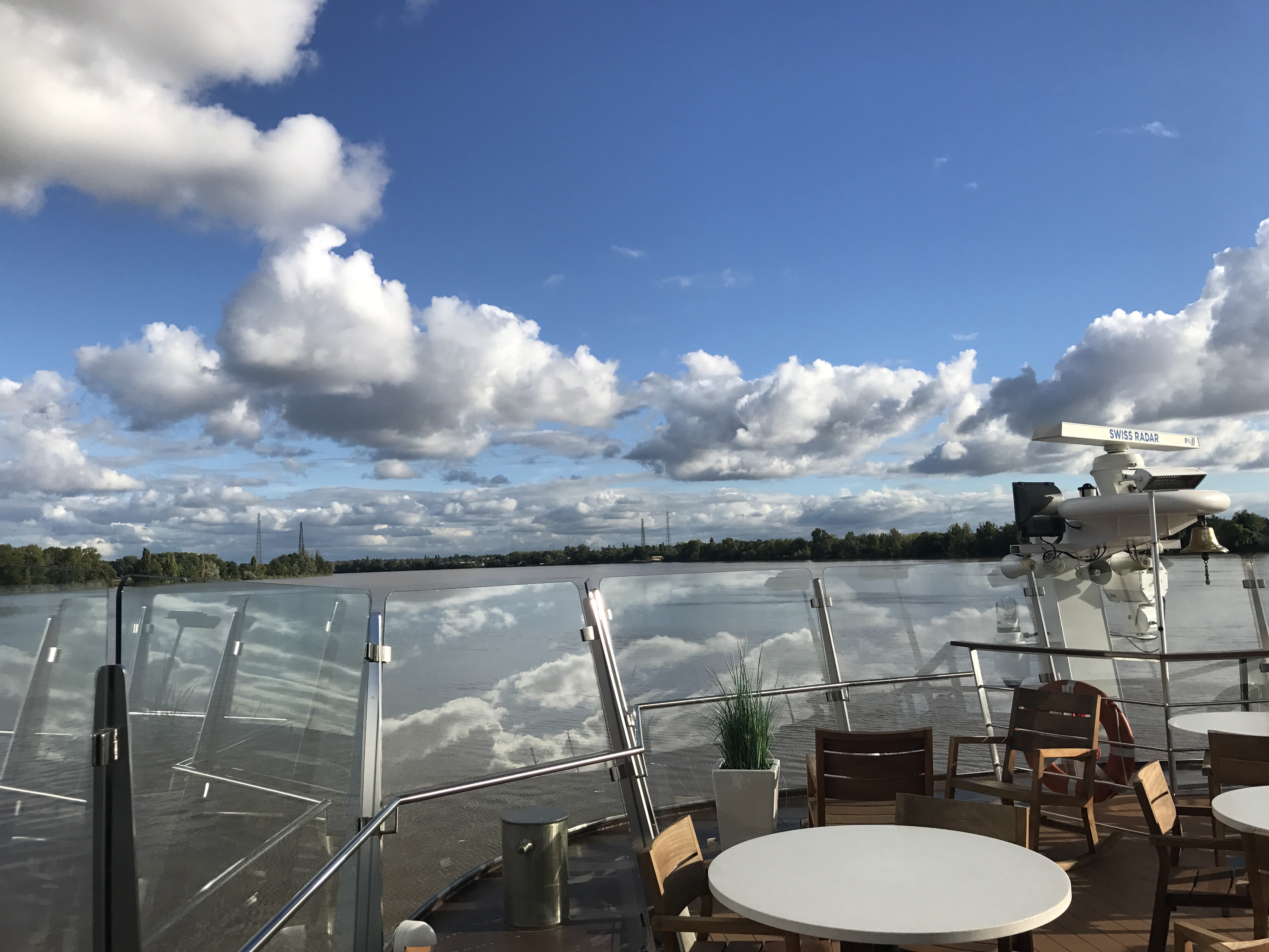 The open top deck of the Forseti behind its glass windbreak, tables set out along the river