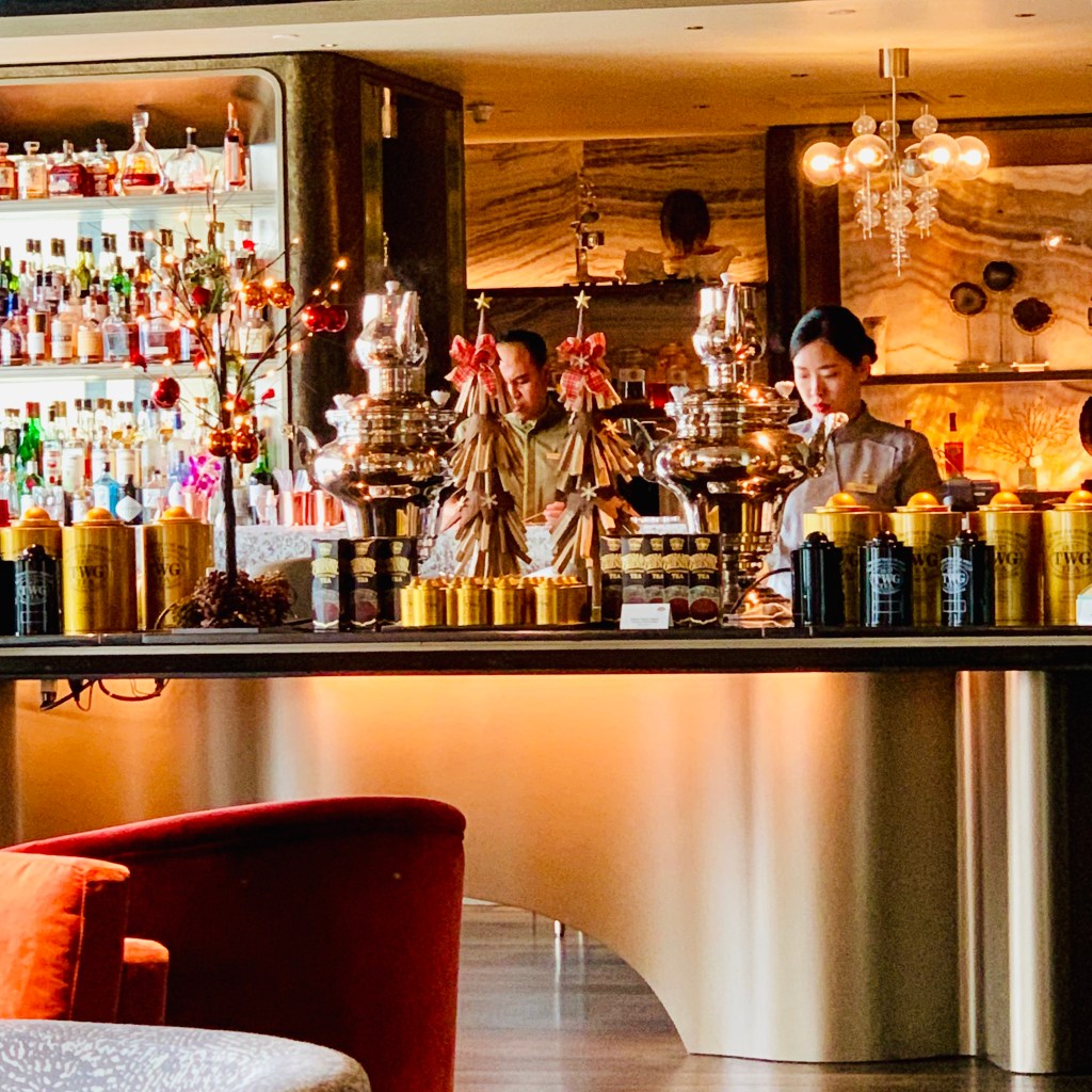 The hotel bar, bottles backlit along the counter and low armchairs in the foreground