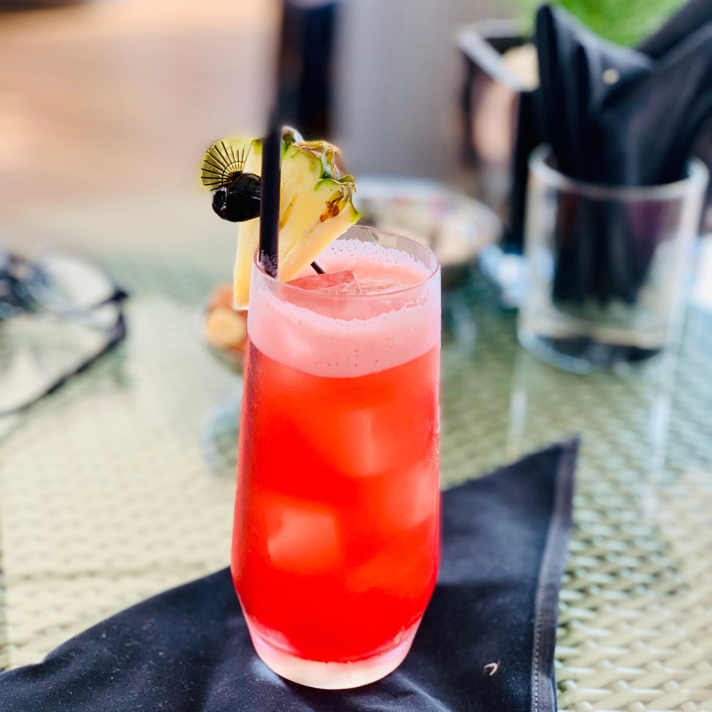 A tall Singapore Sling, pink and cloudy, garnished with a pineapple wedge and a cherry