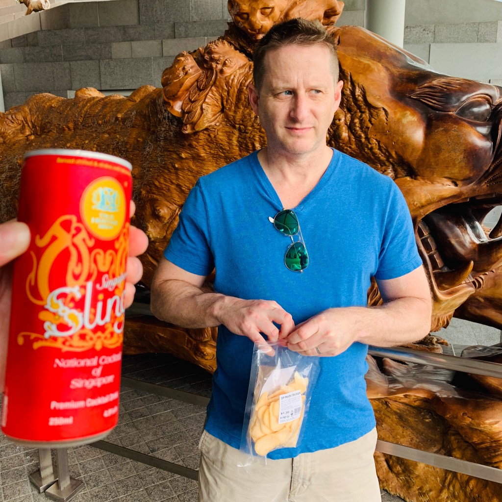 Chris holding a tall red canister of snacks in front of a large gilded sculpture