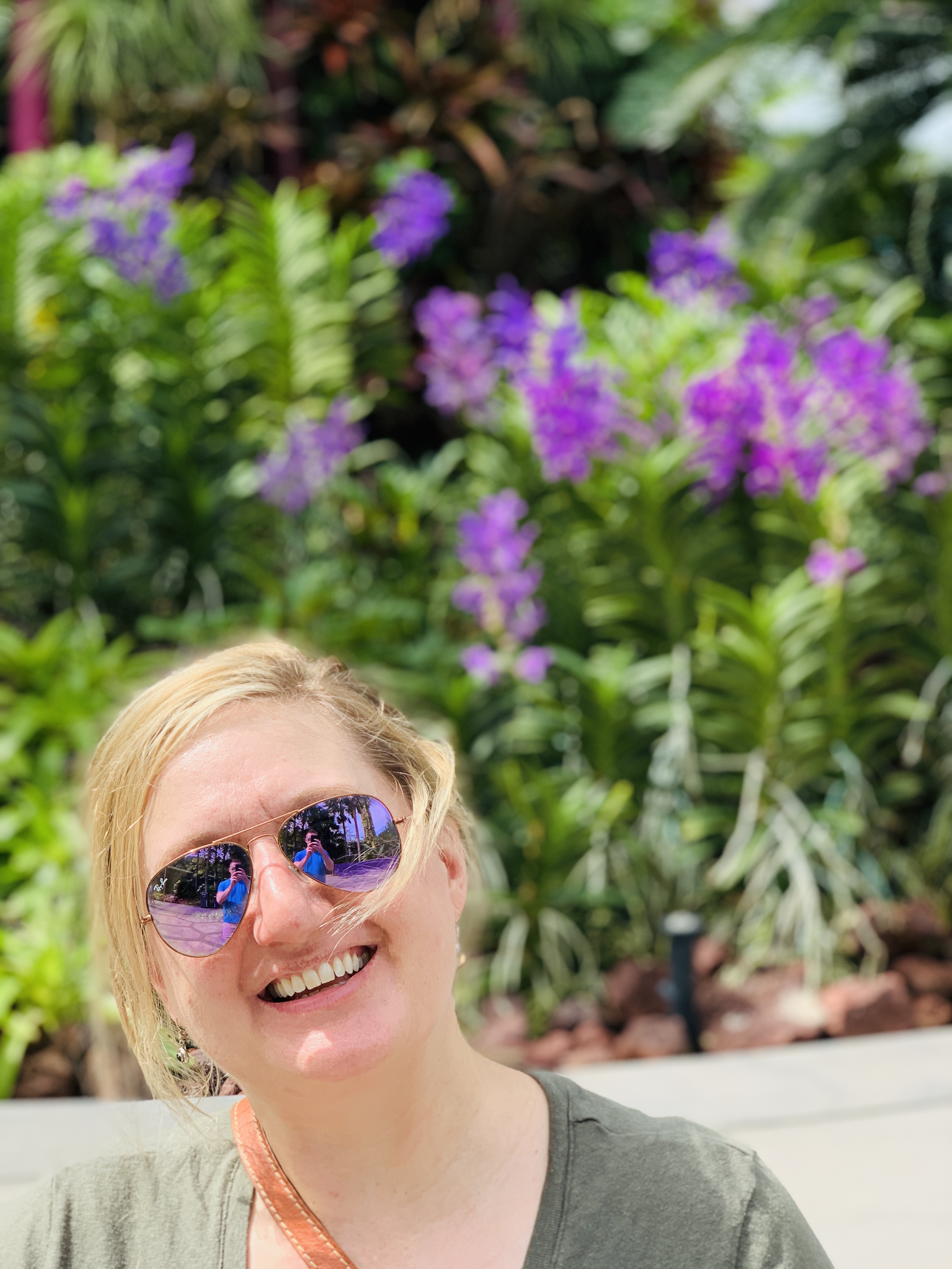Jen in sunglasses beside a stand of purple orchids