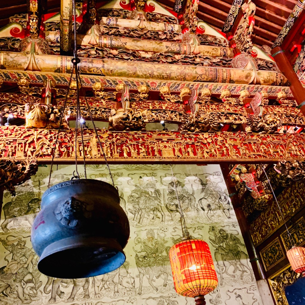 Inside the temple: a great bronze bell below a gilded ceiling, offerings set out beneath