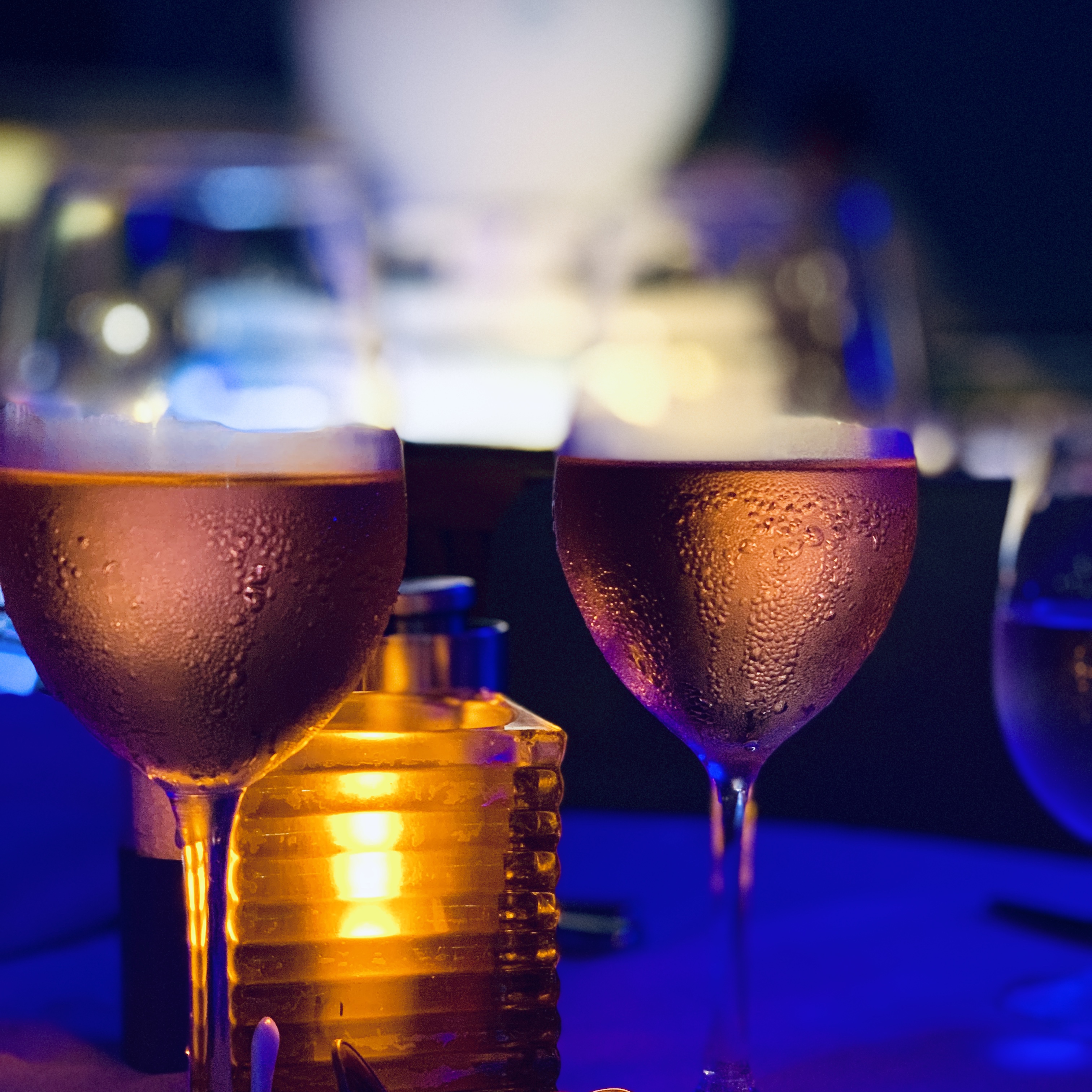 Two amber cocktails in coupe glasses, lit against the blue of the bar