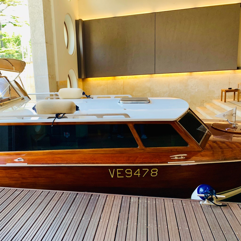 A varnished mahogany Venetian water taxi, registration VE9478, moored alongside a timber dock in front of the hotel lobby.