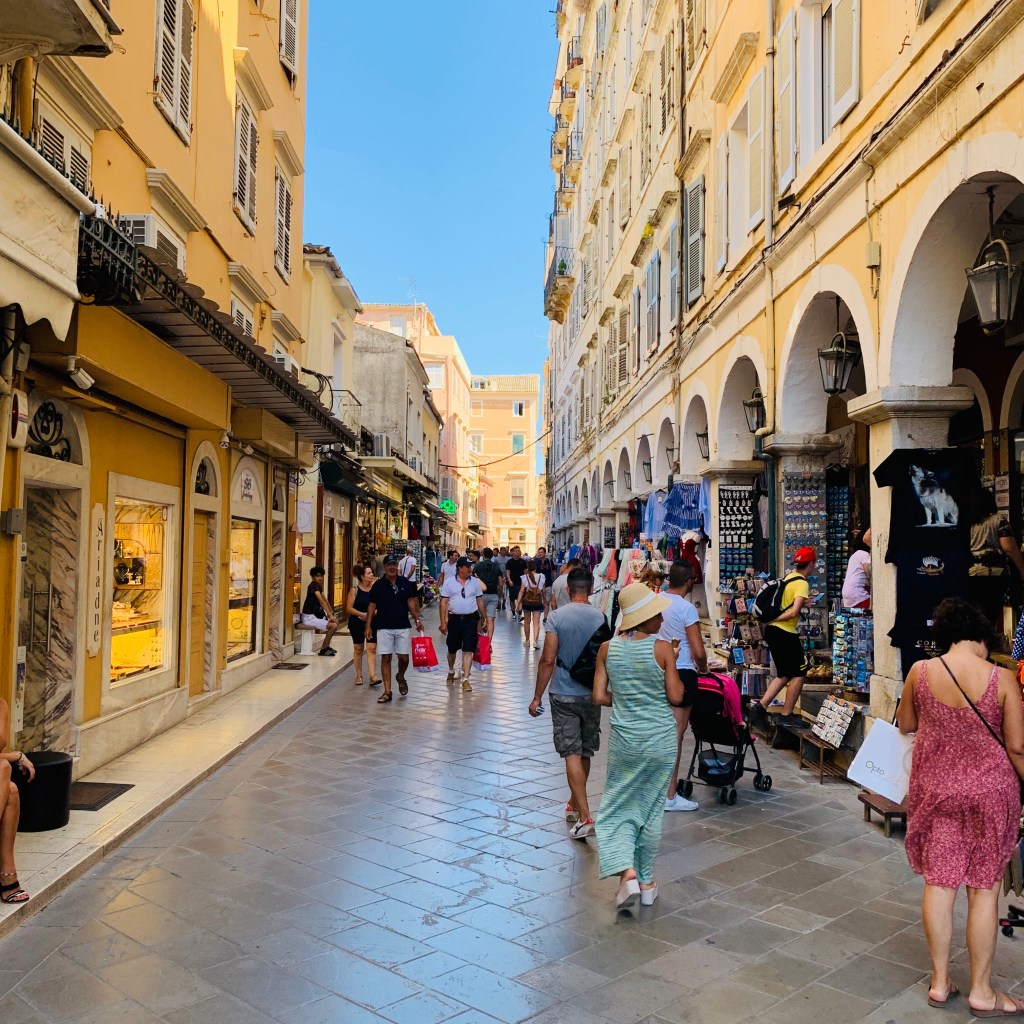 A narrow street in Corfu town running between apartment blocks, with the walls of the Old Fortress on the hill closing off the far end.