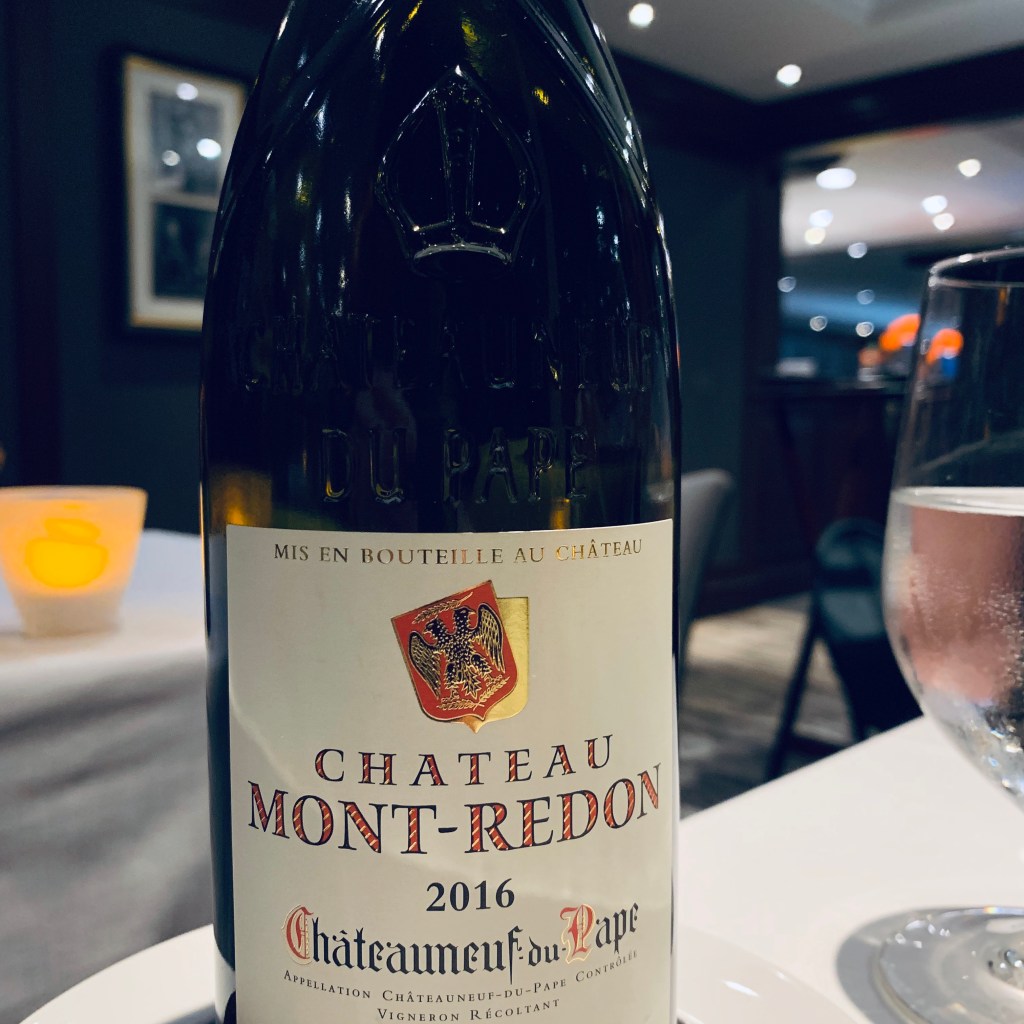 A bottle of Château Mont-Redon 2016 Châteauneuf-du-Pape standing on a white tablecloth in the ship’s restaurant, a wine glass and the cork beside it.