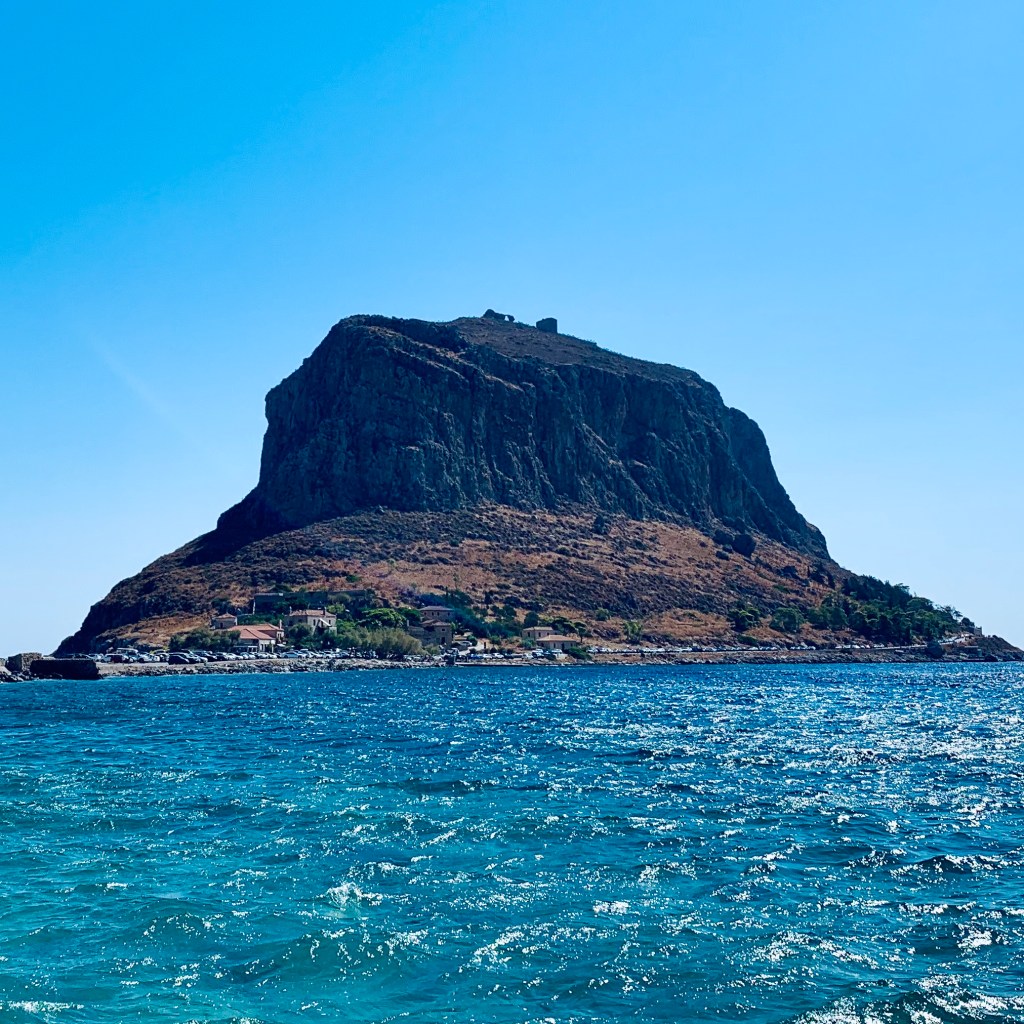 The great rock of Monemvasia rising sheer out of the sea, seen from across the water with the causeway running out to it.