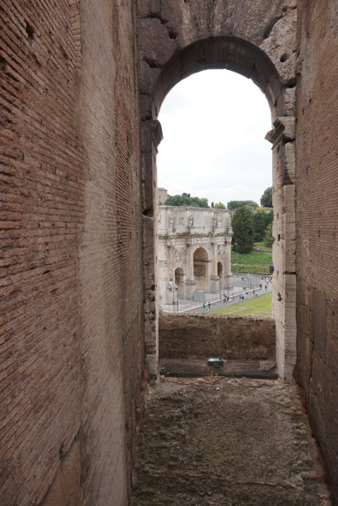 The Arch of Constantine framed through a tall arched opening in the Colosseum wall