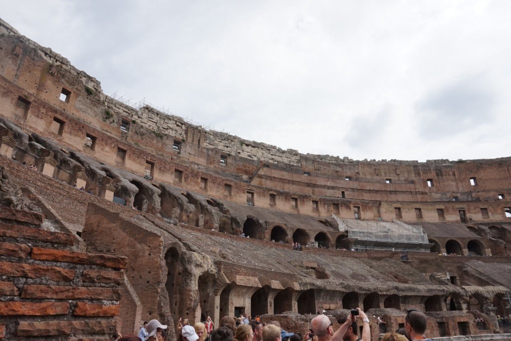 The tiered interior of the Colosseum seen from the first level, visitors along the walkway below