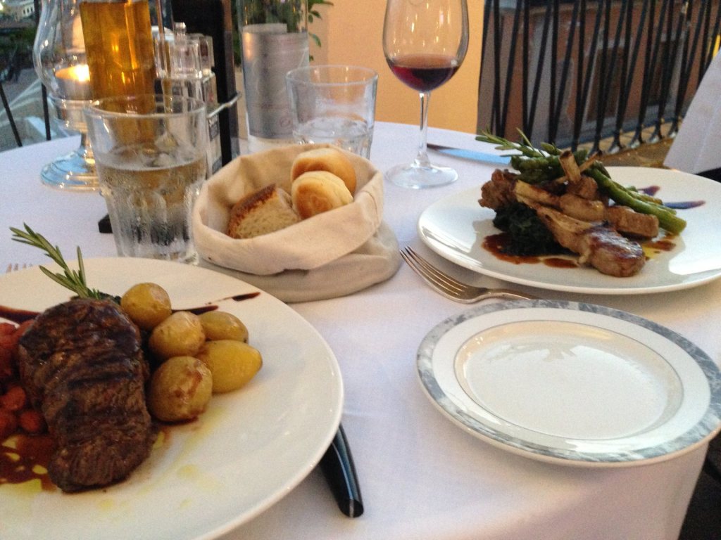 A steak with small roast potatoes, bread in a basket and a glass of red wine on a white cloth