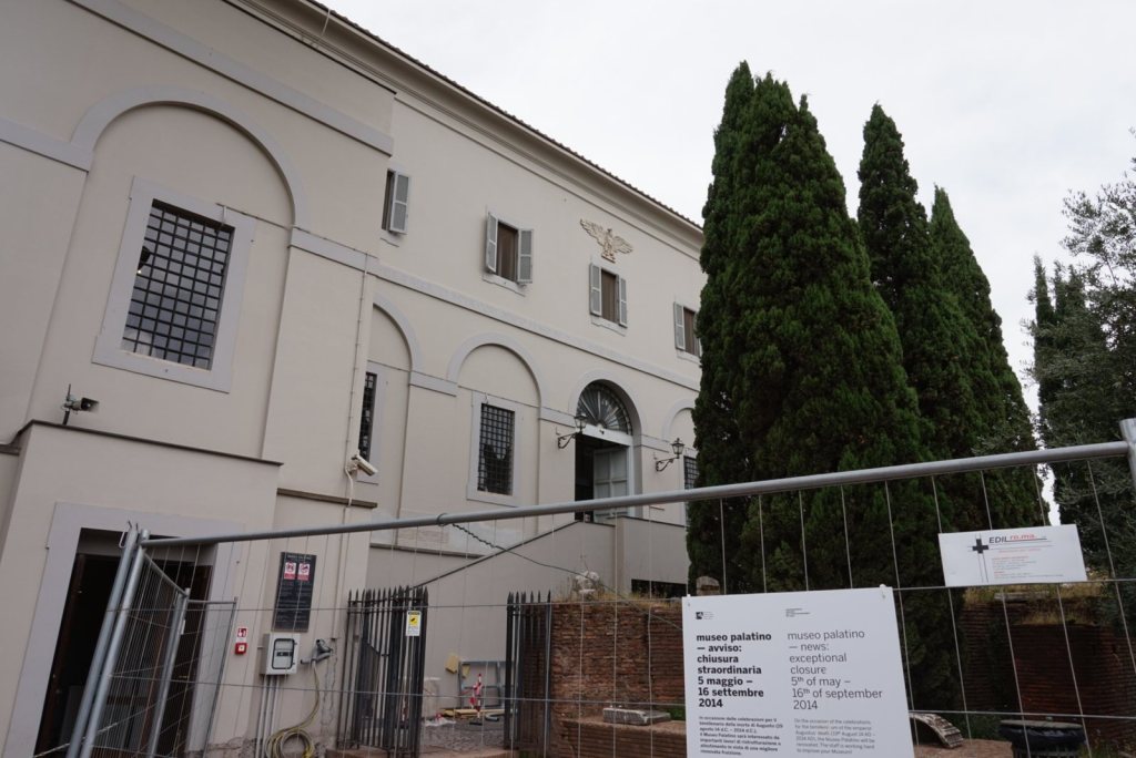 A closure notice posted on the fence outside the Palatine museum, cypresses standing behind