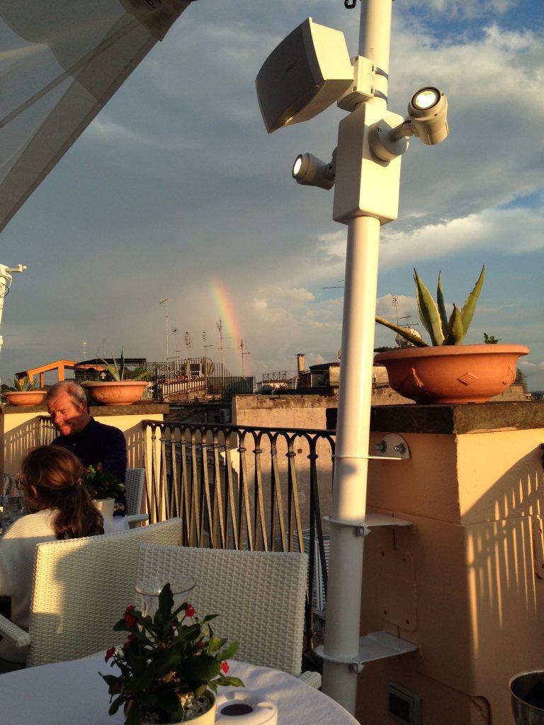 A rainbow over the Rome rooftops seen from a terrace, cloud building behind the domes