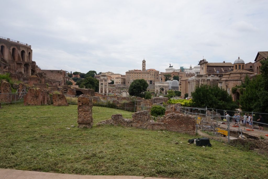 The Roman Forum looking towards the Capitoline, broken walls and grass with the city rising beyond
