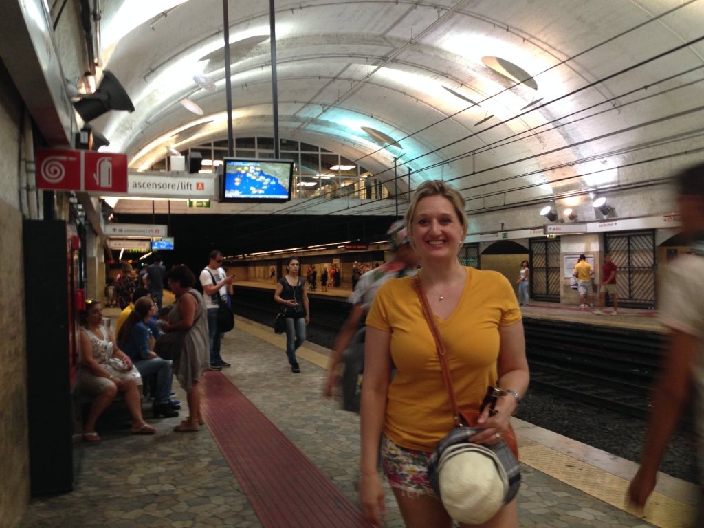 Jen on a Rome Metro platform, a straw hat in her hand and passengers waiting along the tiled wall