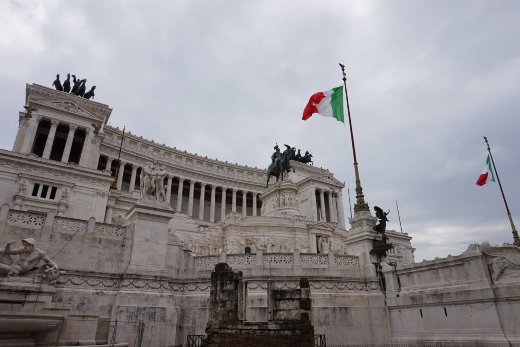 The white marble front of the Vittoriano with the Italian flag flying beside a bronze chariot group