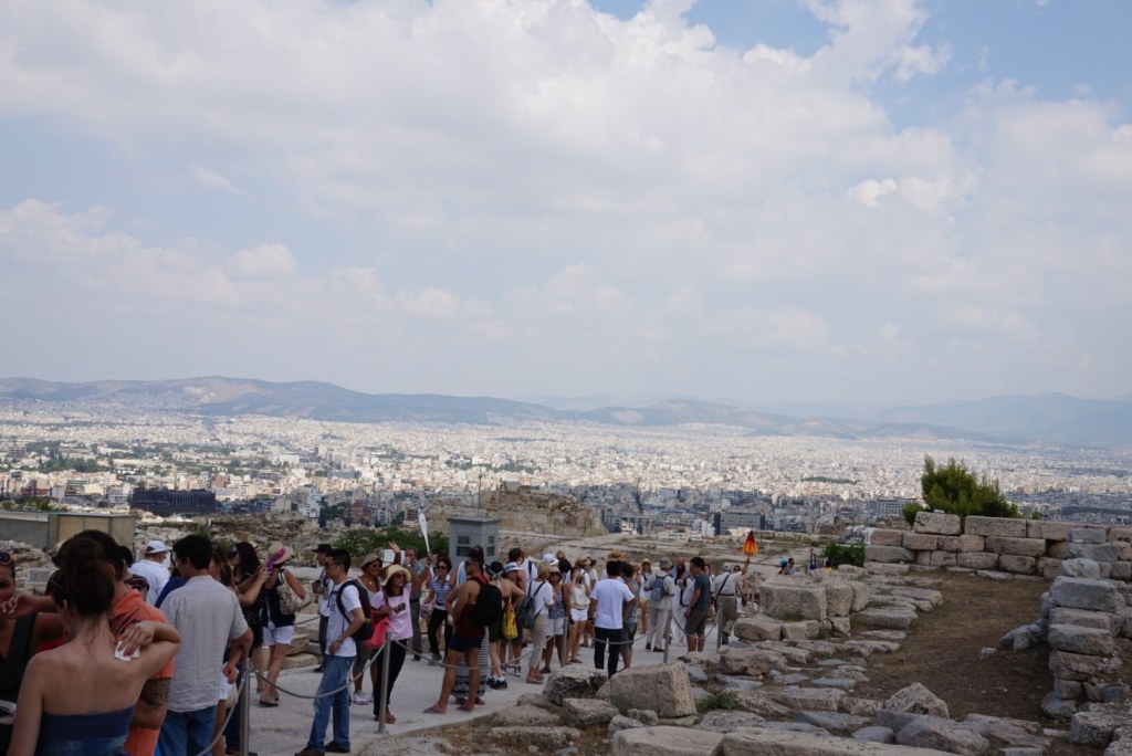 Visitors packed along the path across the Acropolis rock, the white sprawl of Athens and hazy hills beyond