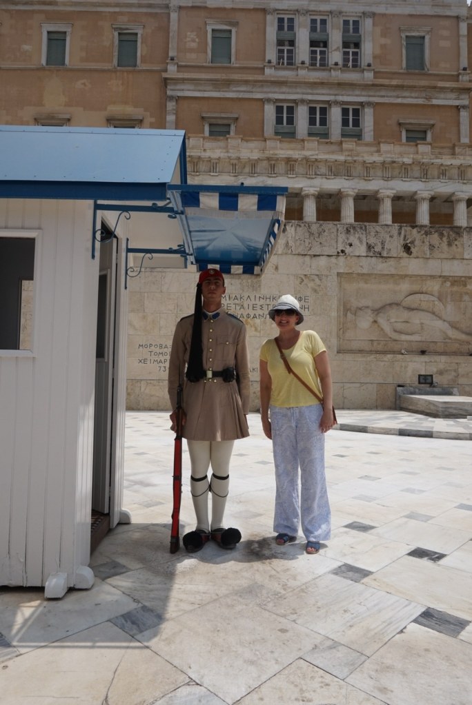 Jen standing beside an Evzone at his sentry box, the guard rigidly at attention